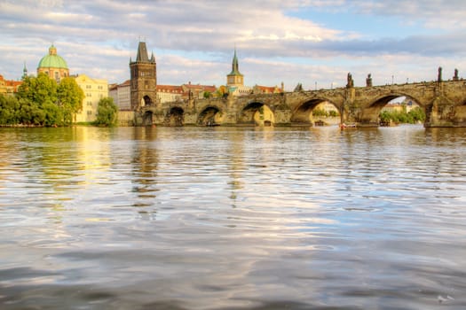 Photo shows the bridge, river and some old houses in Prague.