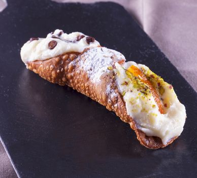 Typical sicilian cannolo, lying over black stone background