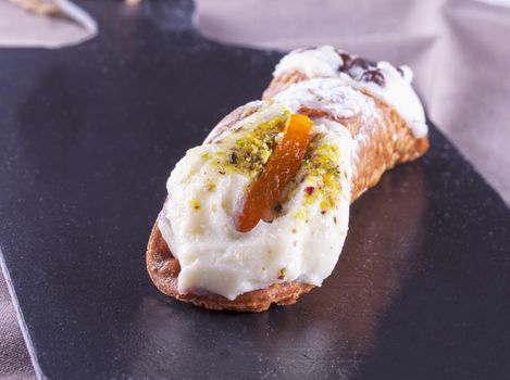 Typical sicilian cannolo, lying over black stone background