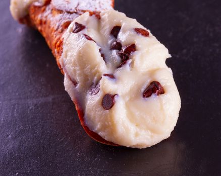 Typical sicilian cannolo, lying over black stone background