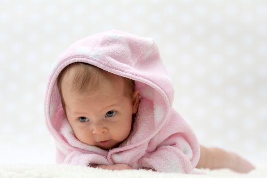 cute little baby girl in pink bathrobe lying on her belly