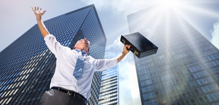 Businessman holding briefcase and cheering against low angle view of skyscrapers