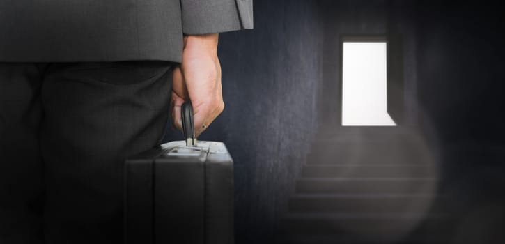 Businessman holding briefcase against grey staircase leading to open door