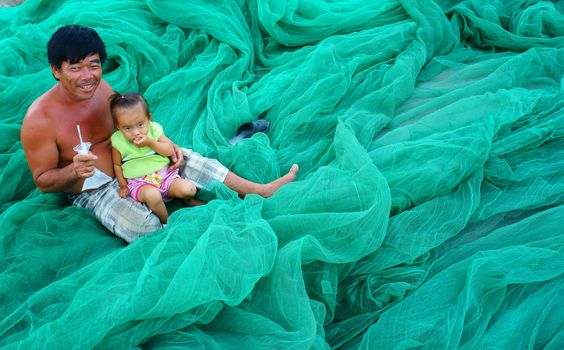 PHAN RANG, VIET NAM- OCT 23: Asian grandfather carry kid, sitting on fishing net at Vietnamese fishing village, happy family with old and young people,  smile face on cyan color, Vietnam, Oct 23, 2014