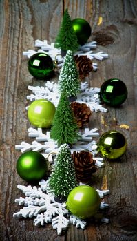 Arrangement of Little Christmas Trees, Green Baubles, Decorative Fir Cones and Snowflake Shapes on Rustic Wooden background