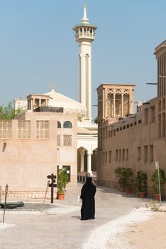 Woman in traditional muslim black dress in old arabic city district with mosque minaret on background