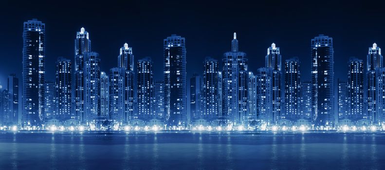 Modern city skyline at night with illuminated skyscrapers over water surface