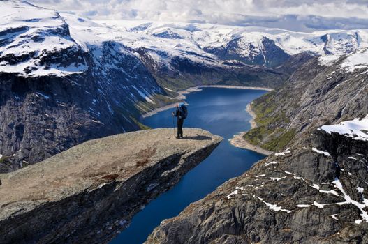Backpacker standing on the sunlit Trolltunga rock, Norway