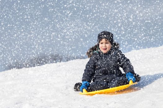 In the snowfall. Boy on sleigh. Sledding at winter time