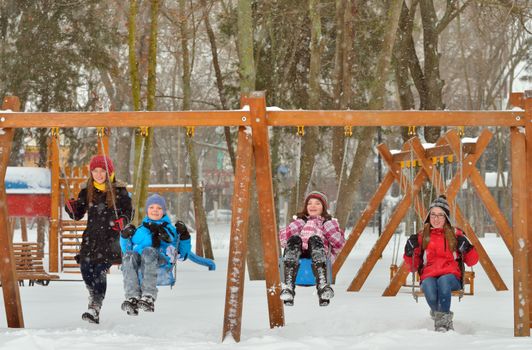 Happy friends sitting on swing in park in winter time