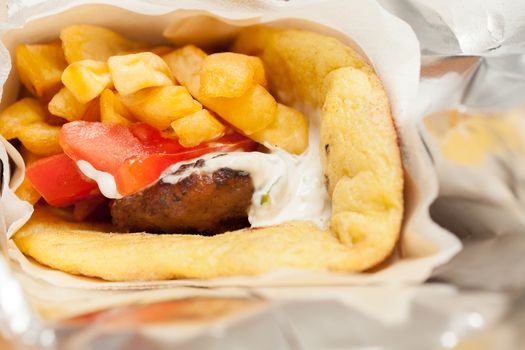 View of a Greek traditional soutzoukaki wrapped with pitta from corn, which contains fried fries, yoghurt, onion and tomato