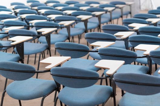 Interior of empty conference hall with blue velvet chairs with small desks for writing notes.