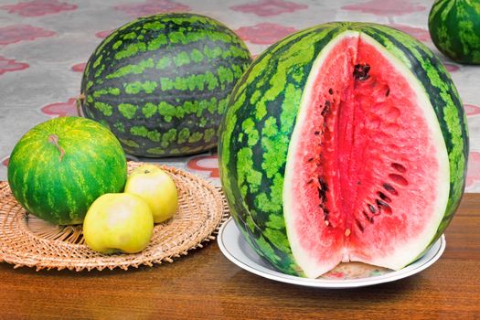 The dish is a large ripe sliced watermelon, near watermelons smaller and apples.