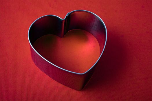 A vintage metal heart shaped sugar dough cookie cutter on red background