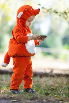 Toddler boy in fox costume holding smartphone outdoors