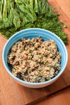 Bowl with Cereal Mix of Red and Whole Grain Quinoa on a wooden surface with dill
