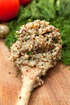 Wooden spoon with ready cooked quinoa, on a wooden surface with dill