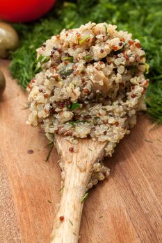 Wooden spoon with ready cooked quinoa, on a wooden surface with dill