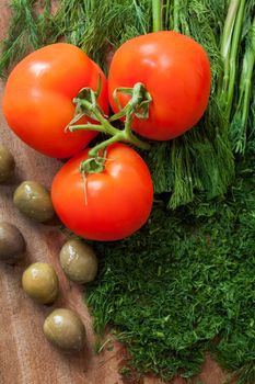 Tomato, dill and olives on wooden surface. Fresh vegetables on a kitchen countertop ready for preparing vegetarian food