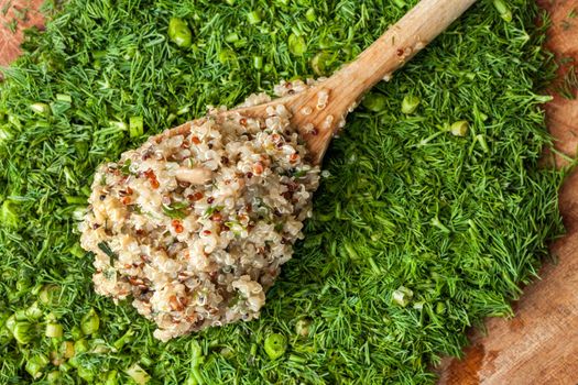 Wooden spoon with ready cooked quinoa, on a wooden surface with dill