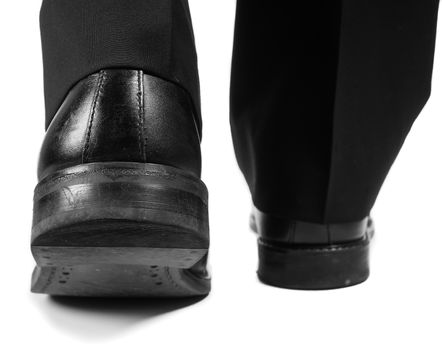 Closeup of male suit walking away in black worn shoes towards white