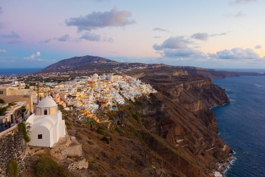 Cityscape of Fira, dramatically located on the edge of the caldera cliff on the island of Thira known as Santorini, Greece. Panorama shot at dusk.