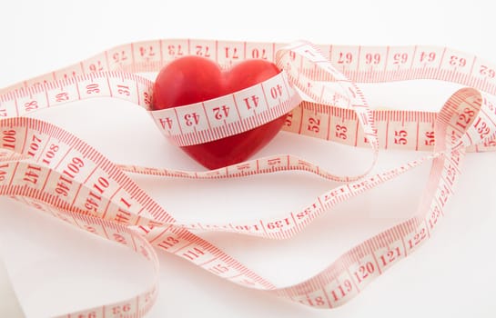 Red heart surrounded by a tape measure on white background