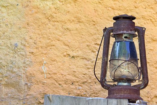 Photo shows rural lantern in front of a yellow wall.