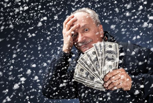 Time to buy gifts. Portrait of a man with a bundle of dollars on a blue background in snowfallPortrait of a man with a bundle of dollars on a blue background in snowfall