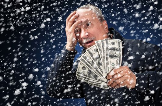 Time to buy gifts. Portrait of a man with a bundle of dollars on a blue background in snowfallPortrait of a man with a bundle of dollars on a blue background in snowfall. Focus on money