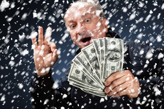 Time to buy gifts. Portrait of a man with a bundle of dollars on a blue background in snowfallPortrait of a man with a bundle of dollars on a blue background in snowfall. Focus on money