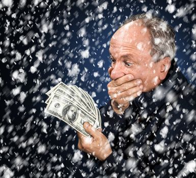 Time to buy gifts. Portrait of a man with a bundle of dollars on a blue background in snowfallPortrait of a man with a bundle of dollars on a blue background in snowfall