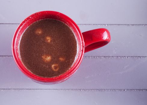 Chocolate and hazelnuts in red cup, over wooden background
