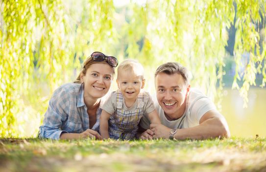 Happy parents with toddler boy. Mother, father and son relaxing on the lawn.