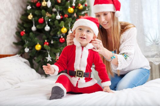Happy mother putting Santa costume on toddler son at home