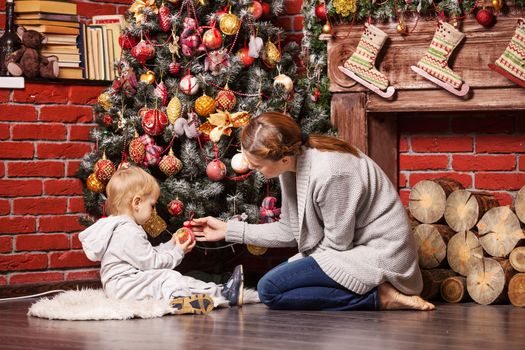 Mother and toddler son holding Christmas ball on Christmas tree at home