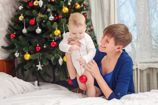 Happy mother and baby boy holding Christmas ball at home