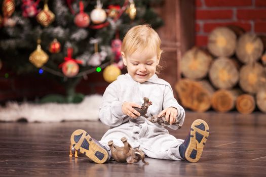 Cheerful little boy playing with his toy animals by Christmas tree