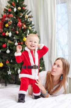 Young mother playing with baby dressed in Santa costume
