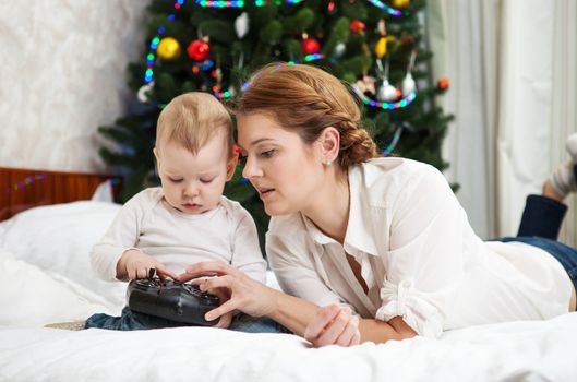 Young Caucasian mother and toddler son playing with RC controller against decorated Christmas tree at home