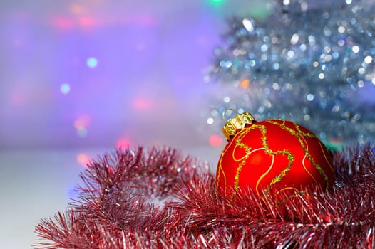 Red Christmas ball under the tree and tinsel on the background lights