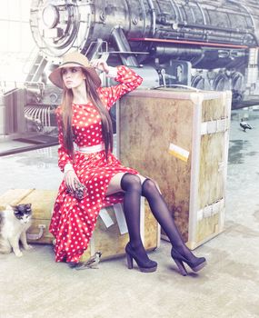 The girl sitting on the suitcase waiting at the retro railway station