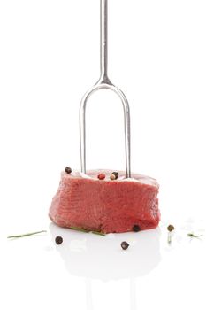 Raw filet mignon on fork steak with herbs and peppercorns isolated on white background. Luxurious red meat steak eating. 