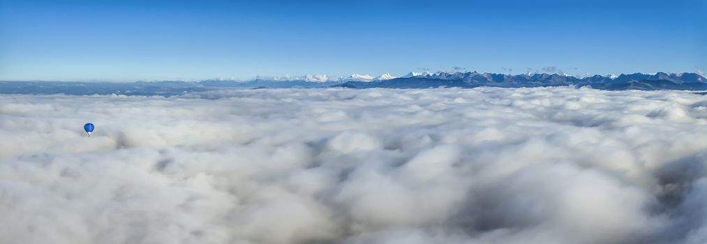 Hot air balloon upon clouds seeing Alps mountains range and deep blue sky, Switzerland