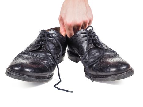 Male hand holding up a pair of worn black leather shoes towards white