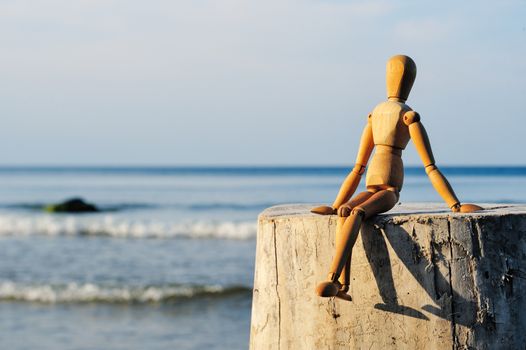 Figurine of wooden man sitting on the stone at the sea