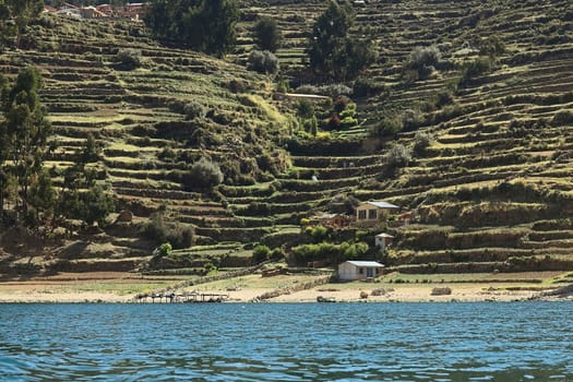 ISLA DEL SOL, BOLIVIA - NOVEMBER 5, 2014: Shoreline with some houses and many old terraces on the hillside on the eastern part of Isla del Sol (Island of the Sun), a popular travel destination in Lake Titicaca, on November 5, 2014 on Isla del Sol, Bolivia  