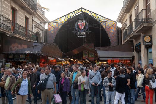 BARCELONA, SPAIN - APRIL 14: Unidentified tourists in famous La Boqueria market with Jamon, vegetables and fruits on April 14, 2012 in Barcelona, Spain. One of the oldest markets in Europe that still exist. Established 1217.