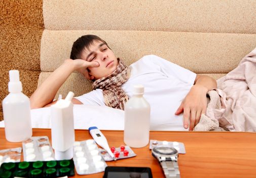 Sad and Sick Teenager on the Sofa at the Home with Pills on foreground