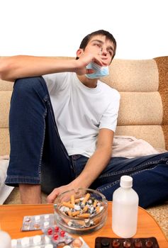 Sick Teenager smoking Cigarette on the Sofa with the Pills on foreground